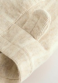 Gros plan d'un moufle en tricot beige doux montrant la section du pouce et les détails du poignet sur un fond clair.