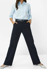 Chemise bleu clair à boutons avec une poche poitrine, associée à un pantalon droit noir marine et des chaussures plates argentées.