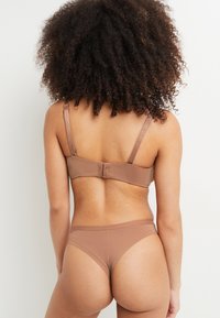Ensemble de lingerie marron sans couture comprenant un soutien-gorge avec des bretelles réglables et une fermeture à crochets, associé à un bas taille basse assorti. Texture lisse.