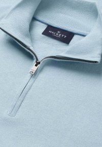 Pull en maille bleu clair avec un col demi-fermeture éclair et une étiquette Hackett London cousue à l'intérieur de l'encolure.