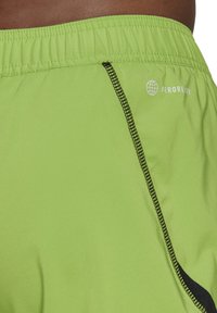 Felle groene sportshorts met een elastische tailleband, voorzien van een zwarte ritszak en het "AEROREADY"-logo. Glad oppervlak en lichtgewicht materiaal.