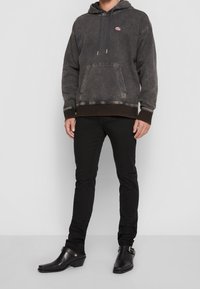 Gray denim hoodie with a front pocket, drawstring hood, and red logo. Paired with slim black pants and black leather heeled boots.