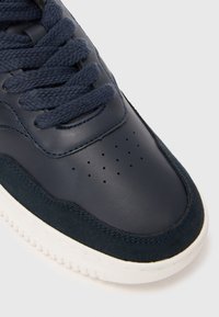 Basket en cuir et en suède bleu marine avec surface texturée, zone des orteils perforée, lacets bleu marine et semelle en caoutchouc blanche.