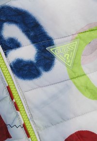 Giacca imbottita con una stampa astratta colorata che presenta forme blu, rosse e verdi. Zip verde neon e logo triangolare visibile.