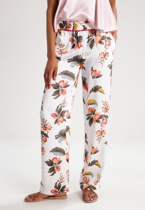 Wijd uitlopende witte broek met oranje, gele en groene bloemenprints, gedragen met een lichtroze top en bruine platte sandalen.