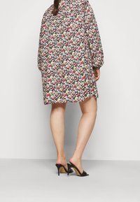 Mekko, jossa on kukkakuosi mustana, löysästi istuva, pitkähihaisilla ja poimutetulla kaula-aukolla, yhdistettynä mustiin korkokenkiin.