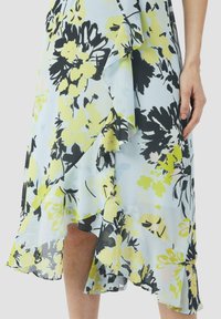 Blumenkleid in Hellblau mit schwarzen und gelben Blumenmustern, ausgestattet mit Rüschen am Saum und unterschiedlichen Texturen im Stoff.