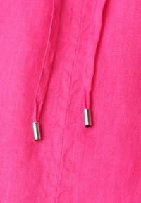 Gros plan d'un tissu rose vif avec deux cordons assortis se terminant par des embouts métalliques argentés.