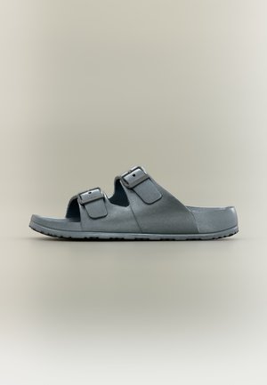 Sandale slide gris foncé avec deux brides réglables à boucle et semelle texturée, vue de profil sur un fond neutre.