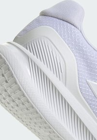 Scarpa sportiva in mesh grigio chiaro con suola testurizzata, soletta bianca liscia e lacci piatti; presenta dettagli a coste sul lato.