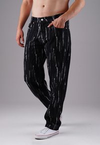 Black denim jeans featuring a vertical striped pattern in gray and white, with five pockets, button closure, and contrasting stitching.