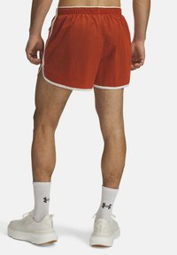 Rote Sportshorts aus strukturiertem Material mit weißen seitlichen Streifen und einem elastischen Bund; getragen mit weißen Socken und Turnschuhen.