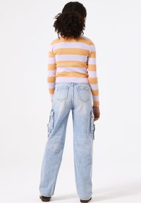 Gestreepte top met lange mouwen in oranje en lavendel, gecombineerd met lichtblauwe cargobroek met zijzakken en een relaxte pasvorm, gezien van de achterkant.