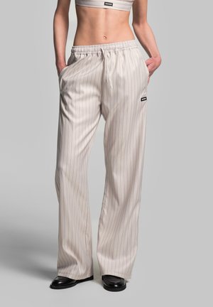 Cream-colored, pinstriped wide-leg trousers with an elastic waistband, side pockets, and a logo patch on the left hip. Smooth texture.