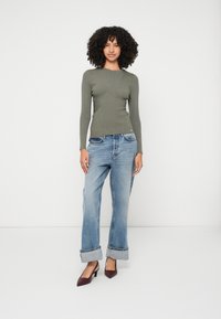 Ελαιώδες ριβέ μακρυμάνικο τοπ, ανοιχτό γαλάζιες παντελόνες φαρδιάς γραμμής με περιλαίμια, και μπορντό τακούνια με αιχμηρή μύτη, με φόντο λευκό.