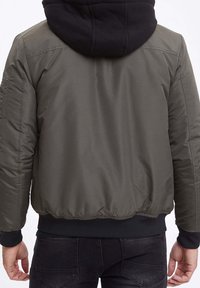 Giacca bomber verde oliva con cappuccio nero, polsini e orlo a costine, dotata di una texture liscia e cuciture visibili sul retro.