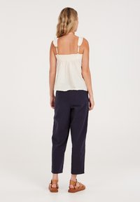 Kremowy top na ramiączkach z marszczonym tyłem, wykończony falbankami, w połączeniu z luźnymi granatowymi spodniami i brązowymi sandałami. Prosty, casualowy design.