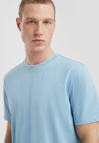 Jasnoniebieska koszulka z okrągłym dekoltem, wykonana z gładkiego materiału, z krótkimi rękawami i luźnym krojem, o subtelnej strukturze i bez widocznych wzorów.