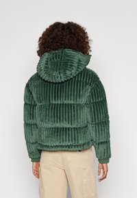 Groene ribfluwelen pufferjack met verticale strepen, met een geribbelde capuchon en elastische manchetten, vanachter weergegeven.