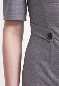 Robe à manches courtes à carreaux gris avec une taille cintrée et un détail de bouton noir sur le côté.