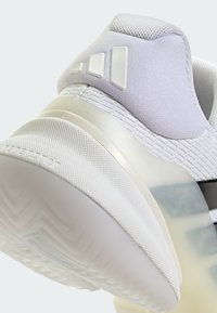 Bílá sportovní obuv s texturovaným svrškem, zesílenou patou a průhlednou pryžovou podrážkou. Obsahuje tři výrazné designové prvky na patě.