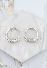 Sölvörhängen med en vriden design prydda med klara rhinestones. Slät metallyta med en polerad finish.