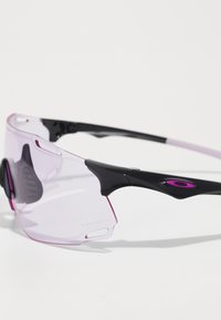 Sportsonnenbrille mit einem eleganten schwarzen Rahmen, pinken Akzenten und einem geschwungenen, verlaufenden, hell-lilanen Glas. Verfügt über Gumminasenpads für besseren Halt.