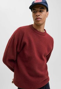 Pull rouge texturé avec encolure ronde et épaules tombantes, associé à une casquette marine. Design simple avec une coupe décontractée.