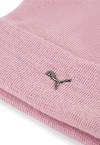 Vaaleanpunainen neulottu pipon, jossa on ribbineulos ja pieni metallinen logoyksityiskohta taitteessa. Pehmeä kangas ja rento muotoilu.