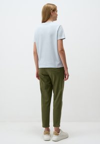 Camicia azzurro chiaro a maniche corte abbinata a pantaloni verde oliva a gamba affusolata, con un fit rilassato e scarpe bianche con un accento beige.