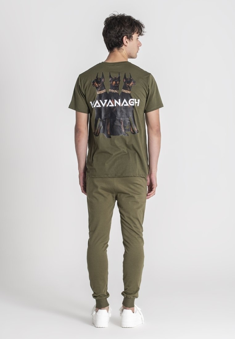 Camiseta verde oliva con un gráfico de tres perros Doberman y el texto "Vavanagh". Pantalones ajustados a juego y zapatillas blancas.