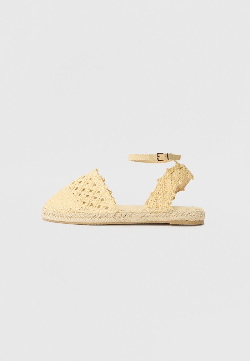 Sandale espadrille tressée beige à bout fermé, bride cheville avec boucle, semelle plate tressée, photographiée sur fond gris clair.
