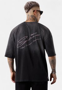 Black oversized t-shirt featuring a gradient design, short sleeves, and pink embroidered text on the back. Cotton material with a relaxed fit.