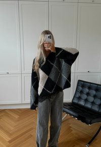 Pulover supradimensionat cu model argyle în nuanțe de negru, gri și bej, cu decolteu în formă de V și țesătură texturată. Asortat cu blugi gri cu pantaloni evazați.