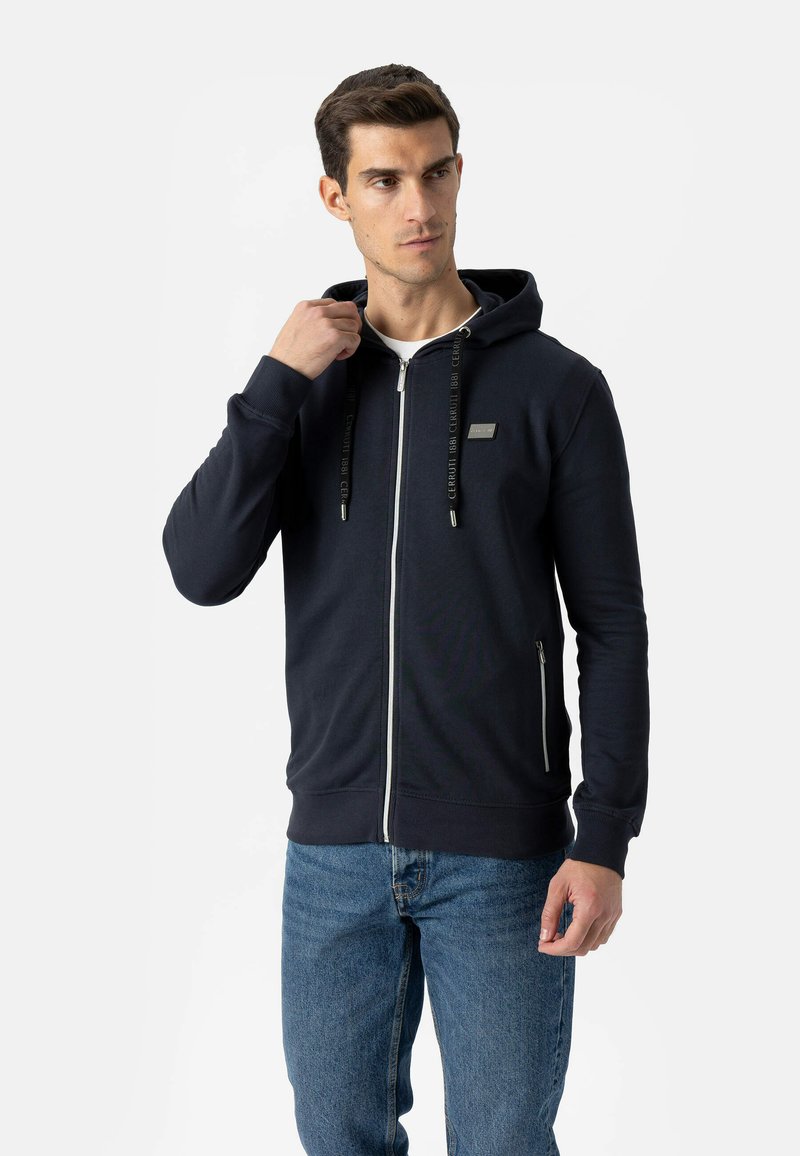Granatowa bluza z kapturem na suwak z srebrnym zamkiem, regulowanymi czarnymi sznurkami i małym logo na piersi. Miękka tkanina i swobodny krój.