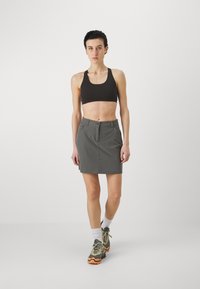 Grå skjørt med en tettsittende design, to frontlommer og knappestengning, kombinert med en svart crop top og flerfargede treningssko.