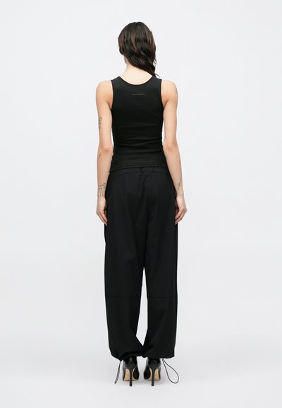 Svart singlet og løstsittende svarte bukser med en jevn tekstur. Buksene har snøring i midjen og er kombinert med høyhælte sko.
