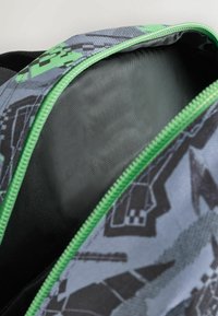 Interior de mochila gris con un zipper verde, mostrando un forro negro texturizado en su interior y un patrón gráfico en el exterior.