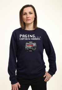 Felpa blu navale con la scritta "PAGING... CAPTAIN MARVEL" e un'immagine di un dispositivo sci-fi con un'emblema rosso e blu e pulsanti di controllo.