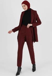 Rood en zwart geruite kostuum met een getailleerde blazer en slim-fit broeken, gecombineerd met een zwarte coltrui en zwarte hakken.