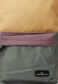 Rygsæk med en gul øverste del, pink detalje lynlås og grøn bund. Lavet af slidstærkt stof med en struktureret overflade og logo-patch.