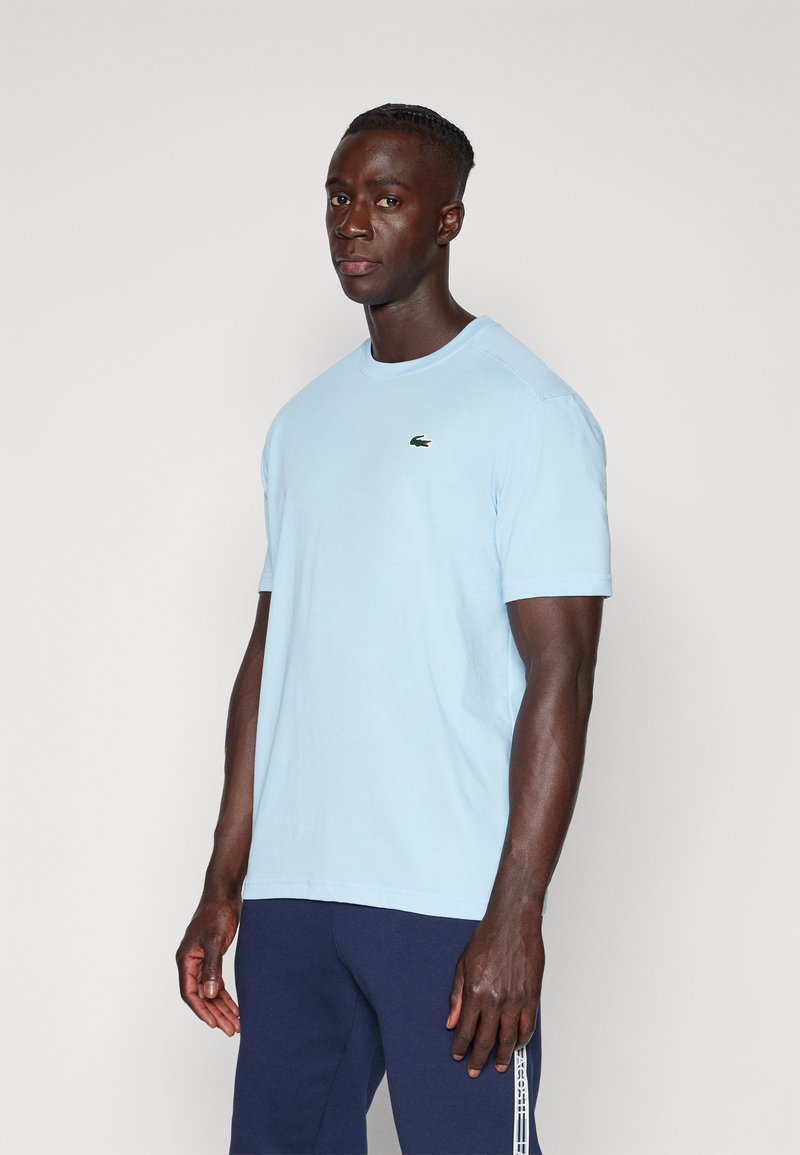 T-shirt di cotone azzurro chiaro con scollo tondo, maniche corte e un piccolo logo verde Lacoste sul lato sinistro del petto.