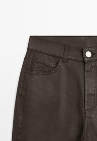 Brown denim pants featuring a standard waistband, front pocket, metal button closure, and smooth texture.