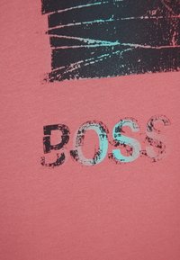 Růžová bavlněná látka s grafickým designem. Slovo "BOSS" je tištěno ve značně opotřebovaném černém a tyrkysovém písmu. Jednoduchá struktura.