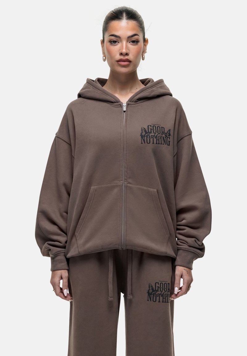 Felpa con zip marrone, dotata di ampie tasche frontali e logo stampato sul petto. Il tessuto è morbido, con una vestibilità rilassata, cappuccio e spalle scese.