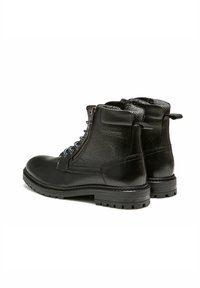 Bottes basses en cuir noir avec fermeture éclair latérale, laçage à l'avant, col rembourré et semelles épaisses en caoutchouc cranté, vues sous un angle arrière latéral.