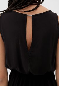 Schwarzes Kleid aus glattem Stoff mit einem Rückenschlitz, der durch eine silberne Hardware-Detail gesichert ist, und einer lockeren, fließenden Silhouette.