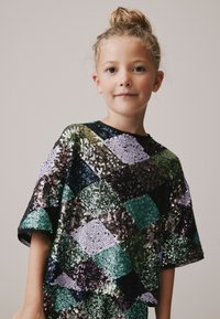 Paljettopp med ett geometriskt diamantmönster i grönt, lila, svart och silver, med korta ärmar och rund halsringning.