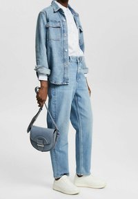 Giacca di jeans azzurro chiaro con due tasche sul petto, camicia bianca, jeans azzurri chiari a vita alta e borsa a tracolla grigia. Sneakers bianche.