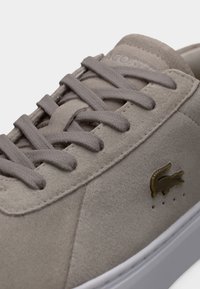 Αθλητικό παπούτσι από γαλλικό καστόρι σε ανοιχτό γκρι χρώμα με επίπεδο κορδόνι, χρυσή λεπτομέρεια λογότυπου και λευκή λαστιχένια σόλα. Υλικό με υφή και ραμμένες ραφές.